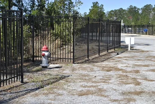 Tall gated fence around storage facility, near fire hydrant.